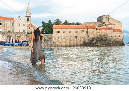Woman Standing In Adriatic Sea With Bell Tower Of Sveti Ivana Cathedral On Background In Budva, Mont