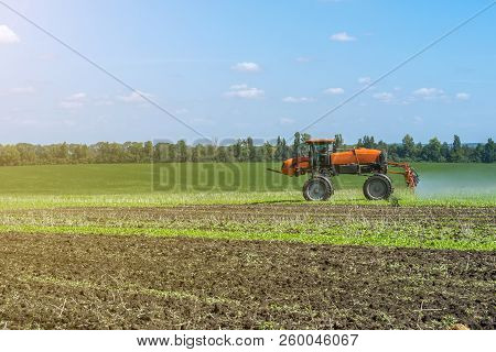 Self-propelled Sprayer Works On A Field Under A Blue Sky With Clouds