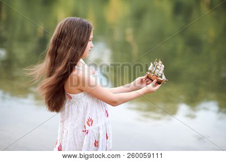 girl playing with a toy sailing ship by the river