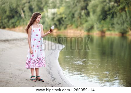 girl playing with a toy sailing ship by the river