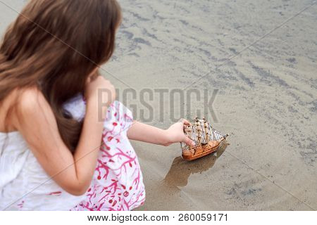 girl playing with a toy sailing ship by the river