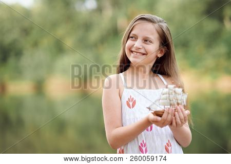 girl playing with a toy sailing ship by the river