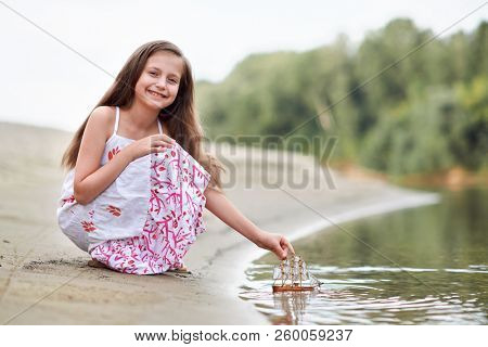 girl playing with a toy sailing ship by the river