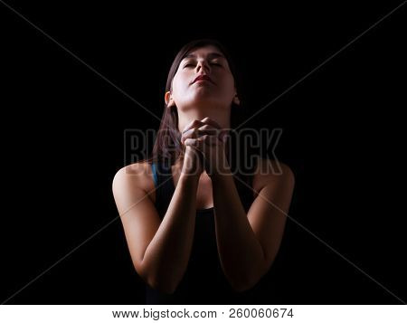 Faithful woman praying, hands folded in worship to god with head up and closed eyes in religious fervor, on a black background. Concept for religion, faith, prayer and spirituality.