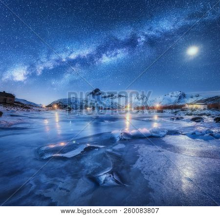 Milky Way Above Frozen Sea Coast, Snow Covered Mountains And Starry Sky With Moon In Winter At Night