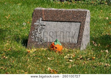 Halloween Jack O Lantern Decoration By Grave Tombstone With Fallen Autumn Leaves On Grass