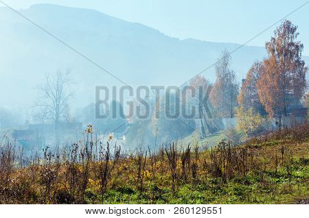 Autumn Carpathian Mountains Landscape With Multicolored Trees And Small Hamlet On Slope, And Misty C