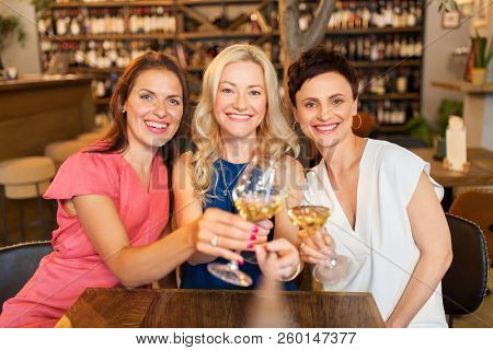 people, celebration and lifestyle concept - happy women drinking wine and clinking glasses at bar or restaurant