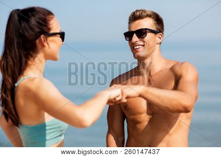 fitness, sport and lifestyle concept - happy couple in sports clothes and sunglasses on beach making fist bump gesture