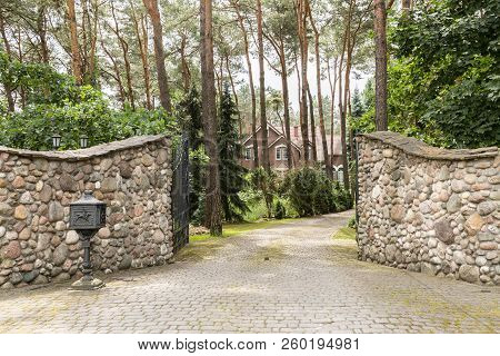 Entrance Gate To A Rustic, English House In The Forest With Stone Wall And Cobblestone Driveway