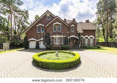 Front View Of A Driveway With A Round Garden And Big, English Style House In The Background. Real Ph