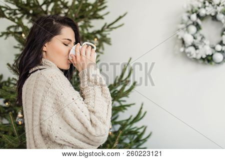 Horizontal Shot Of Beautiful Young Bruntte Woman Posing At Home With A Mug Of Hot Tea Next To The Ch