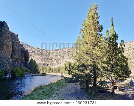 The Beautiful Crooked River With Fall Colored Bushes On Its Banks Flows Through A Canyon Formed From