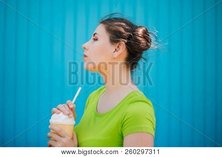 Portrait Of A Girl Against A Bright Blue Wall. Emotional Girl Holding A Plastic Glass With A Refresh