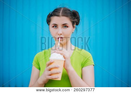 Portrait Of A Girl Against A Bright Blue Wall. Emotional Girl Holding A Plastic Glass With A Refresh