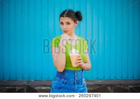 Portrait Of A Girl Against A Bright Blue Wall. Emotional Girl Holding A Plastic Glass With A Refresh