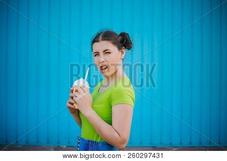 Portrait Of A Girl Against A Bright Blue Wall. Emotional Girl Holding A Plastic Glass With A Refresh