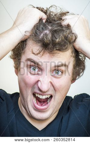 Portrait Of Young Angry Screaming Curly Man Tears His Hair Out On White Background.