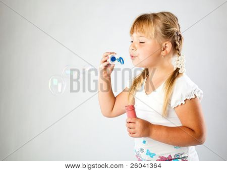 Nuori tyttö puhaltaa saippuakuplia harmaa tausta