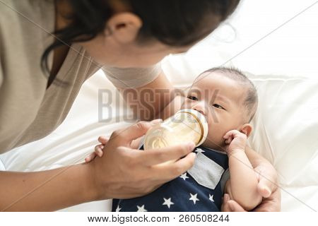 Young Hispanic Baby Or Asian Infant Boy Drinking Milk From Plastic Bottle Feeding From Young Parents