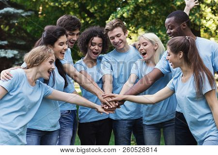Happy Young Diverse Volunteers Preparing For Work, Join Hands In Park. Volunteering And Teambuilding
