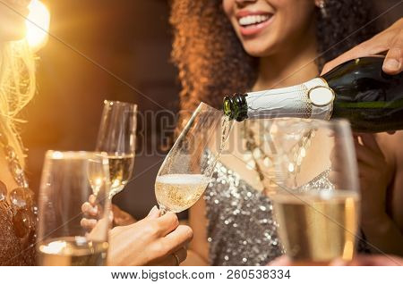 Hand pouring champagne from bottle into glasses with friends around him. Closeup of hand pouring white wine in flutes during party. Detail shot of new yearâs eve celebration.
