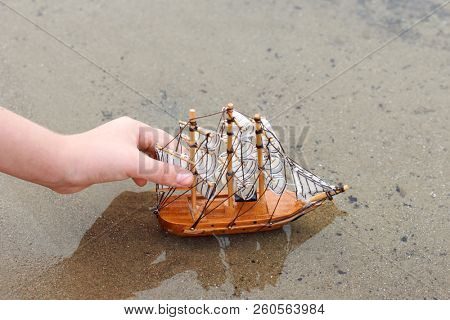 girl playing with a toy sailing ship by the river, hand closeup