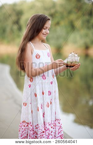 girl playing with a toy sailing ship by the river