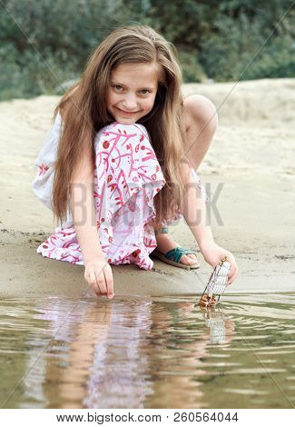 girl playing with a toy sailing ship by the river