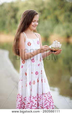 girl playing with a toy sailing ship by the river
