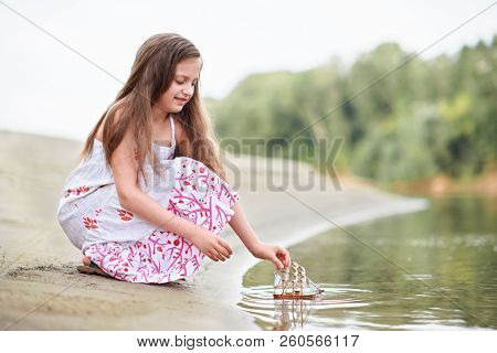 girl playing with a toy sailing ship by the river