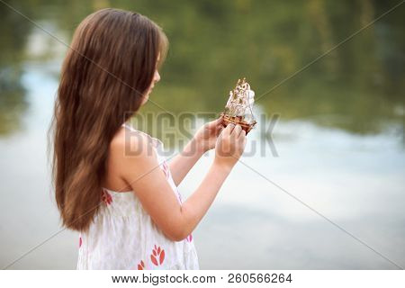 girl playing with a toy sailing ship by the river