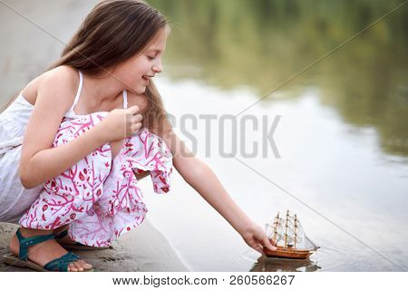 girl playing with a toy sailing ship by the river