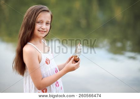 girl playing with a toy sailing ship by the river
