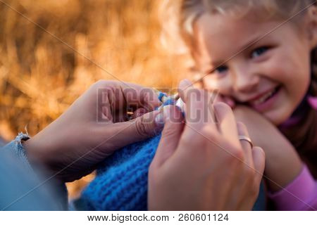 Close-up Of A Young Woman Knitting With Her Knitting Blue Cap Made Of Natural Wool, In The Backgroun