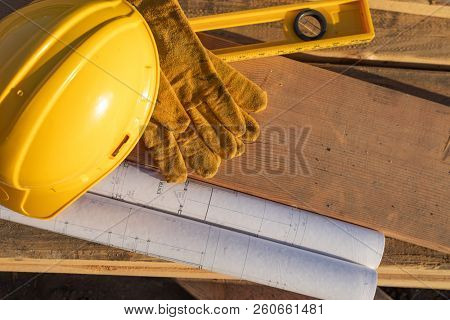Abstract of Constrcution Hard Hat, Gloves, Level and House Plans Resting on Wood Planks.