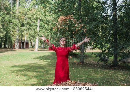 Young Woman In Red Dress. Toss The Autumn Leaves Upward.