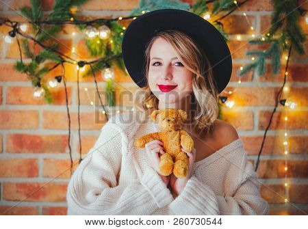 Portrait Of A Young Cozy Woman In White Sweater With Teddy Beartoy And Christmas Lights On Backgroun