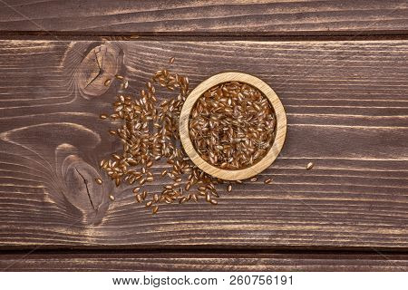 Lot Of Whole Fresh Brown Flaxseeds With Wooden Bowl Flatlay On Brown Wood