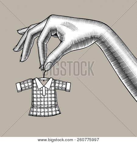 Female hand holding a tiny little dress on hanger. Symbol and metaphor of tailoring. Vintage engraving stylized drawing