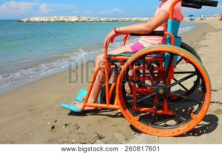 Little Girl On The Wheelchair With Special Metal Wheels To Go On The Beach By The Sea