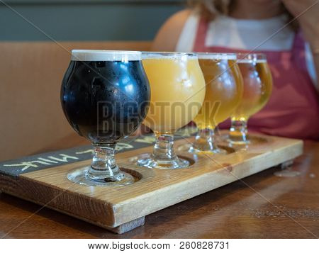 A  Flight Of Stout, Amber, Ipa Beers Sitting On Wooden Paddle
