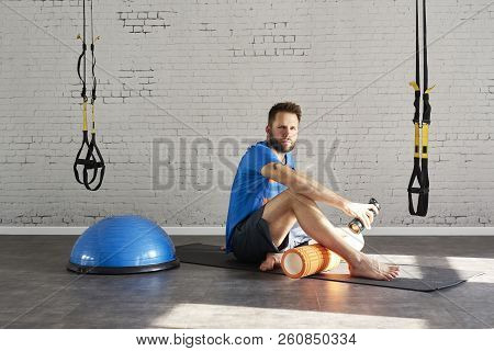 Handsome Muscular Man Athlete Sitting In Sunny Sport Club, Relaxed After Workout, Holding Bottle Of 
