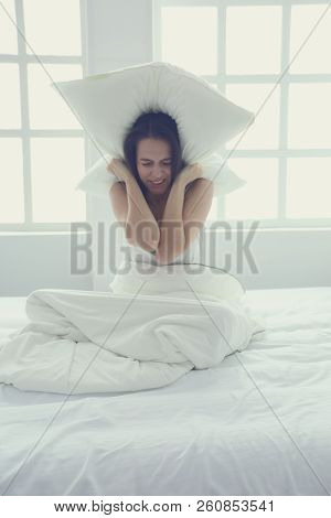Young Caucasian Woman Covering Her Head And Ears With Pillows.