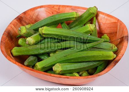Whole Raw Okra In A Wooden Bowl Against A White Background