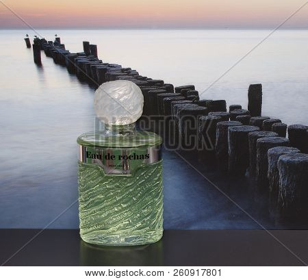 Eau De Rochas, Fragrance For Ladies, Large Perfume Bottle In Front Of The Picture Of A Groyne In The