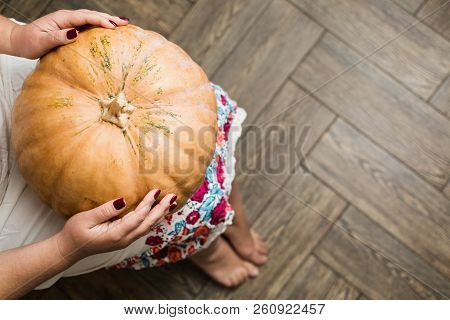 Young Woman In White Dress Holding A Big Pumpkin On Her Lap.