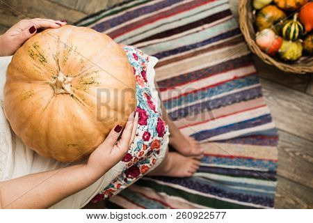 Young Woman In White Dress Holding A Big Pumpkin On Her Lap.