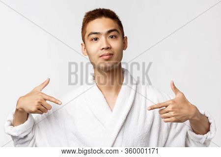 Beauty, Spa And Leisure Concept. Portrait Of Confident, Upbeat Smiling Asian Man In Bathrobe, Pointi