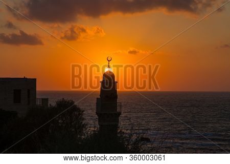 Round tower crowned with a crescent is a Muslim minaret. The setting sun plunges into the Mediterranean Sea. Old Yaffo, Tel Aviv. Concept active, informative and photo of tourism